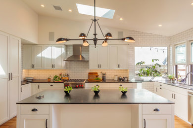 Mid-sized cottage u-shaped light wood floor eat-in kitchen photo in Los Angeles with a single-bowl sink, shaker cabinets, white cabinets, soapstone countertops, white backsplash, subway tile backsplash, stainless steel appliances, an island and black countertops
