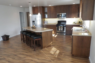 Inspiration for a mid-sized timeless l-shaped medium tone wood floor eat-in kitchen remodel in Seattle with a drop-in sink, recessed-panel cabinets, dark wood cabinets, solid surface countertops, white backsplash, stainless steel appliances and an island
