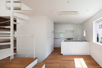 Inspiration for a mid-sized modern galley eat-in kitchen in Tokyo with an undermount sink, flat-panel cabinets, white cabinets, stainless steel benchtops, white splashback, with island, brown floor, stainless steel appliances and painted wood floors.