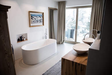 Mittelgroßes Modernes Badezimmer En Suite mit freistehender Badewanne, weißer Wandfarbe, Betonboden, Aufsatzwaschbecken, Waschtisch aus Holz, grauem Boden und brauner Waschtischplatte in München