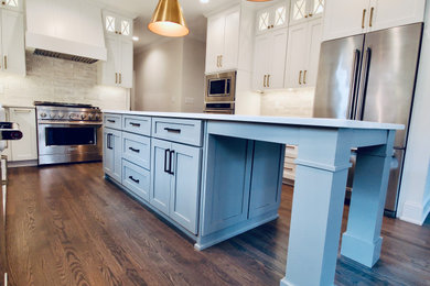 Design ideas for a large eclectic u-shaped eat-in kitchen in Raleigh with a farmhouse sink, shaker cabinets, white cabinets, solid surface benchtops, white splashback, ceramic splashback, stainless steel appliances, medium hardwood floors, with island and white benchtop.