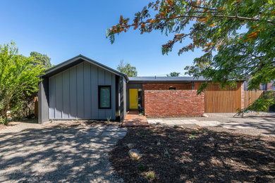 Cette photo montre une petite façade de maison grise tendance de plain-pied avec un toit à deux pans, un toit en métal et un toit noir.