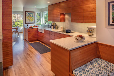Inspiration for a mid-sized 1960s u-shaped medium tone wood floor kitchen pantry remodel in Seattle with a farmhouse sink, flat-panel cabinets, medium tone wood cabinets, quartz countertops, white backsplash, ceramic backsplash, paneled appliances and white countertops