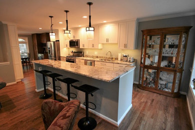 Bild på ett mellanstort vintage kök, med en undermonterad diskho, släta luckor, vita skåp, granitbänkskiva, rostfria vitvaror, mellanmörkt trägolv, en köksö och brunt golv
