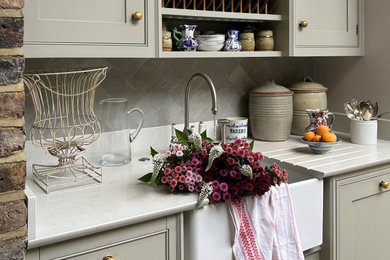 Inspiration for a medium sized classic grey and black galley open plan kitchen with a belfast sink, beaded cabinets, grey cabinets, engineered stone countertops, grey splashback, ceramic splashback, black appliances, marble flooring, an island, grey floors, grey worktops and a feature wall.