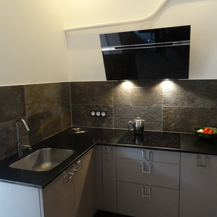 Новые идеи обустройства дома: маленькая п-образная кухня-гостиная в стиле лофт с одинарной раковиной, фасадами с декоративным кантом, коричневыми фасадами, столешницей из кварцита, серым фартуком, фартуком из сланца, техникой из нержавеющей стали, полом из керамической плитки, серым полом и черной столешницей без острова