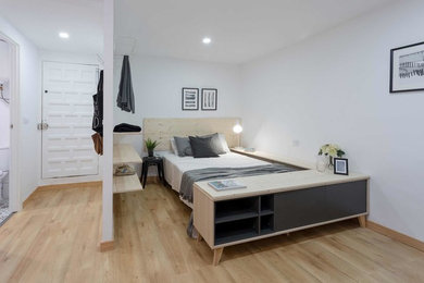 This is an example of a contemporary master bedroom in Madrid with white walls and brown floor.