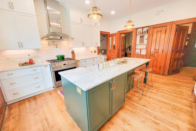 Mid-sized elegant galley medium tone wood floor and brown floor eat-in kitchen photo in Other with a farmhouse sink, recessed-panel cabinets, white cabinets, granite countertops, white backsplash, ceramic backsplash, stainless steel appliances, an island and white countertops