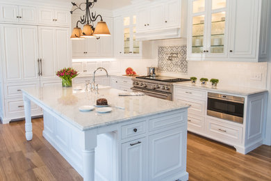 This is an example of a mid-sized traditional l-shaped eat-in kitchen in Detroit with a farmhouse sink, beaded inset cabinets, white cabinets, marble benchtops, white splashback, ceramic splashback, stainless steel appliances, medium hardwood floors, with island and white benchtop.