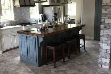 Example of a mid-sized transitional galley brick floor and gray floor enclosed kitchen design in Other with an undermount sink, raised-panel cabinets, white cabinets, wood countertops, gray backsplash, matchstick tile backsplash, stainless steel appliances, an island and white countertops