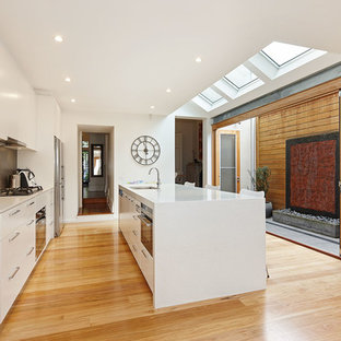 Inspiration for a mid-sized contemporary galley eat-in kitchen in Other with flat-panel cabinets, white cabinets, grey splashback, ceramic splashback, stainless steel appliances, medium hardwood floors, brown floor, an undermount sink and with island.