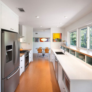 Создайте стильный интерьер: маленькая отдельная, параллельная кухня в современном стиле с двойной раковиной, плоскими фасадами, белыми фасадами, столешницей из дерева, синим фартуком, фартуком из керамической плитки, техникой из нержавеющей стали, пробковым полом, оранжевым полом и белой столешницей без острова - последний тренд