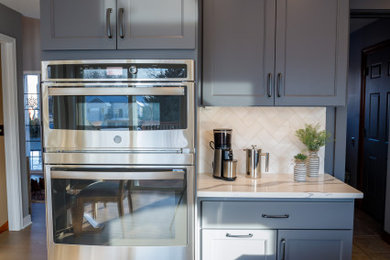 ミネアポリスにあるお手頃価格の広いトランジショナルスタイルのおしゃれなキッチン (エプロンフロントシンク、落し込みパネル扉のキャビネット、青いキャビネット、クオーツストーンカウンター、白いキッチンパネル、磁器タイルのキッチンパネル、シルバーの調理設備、無垢フローリング、茶色い床、白いキッチンカウンター) の写真