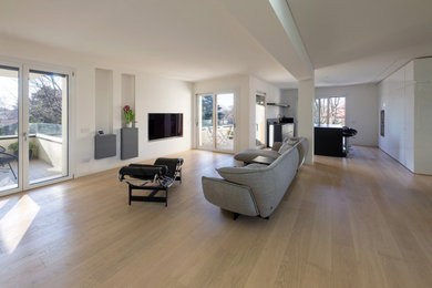 Diseño de salón abierto moderno extra grande con paredes blancas, suelo de madera clara y televisor colgado en la pared