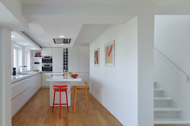 Mittelgroße, Offene Moderne Küche in L-Form mit flächenbündigen Schrankfronten, weißen Schränken, Küchenrückwand in Weiß, Küchengeräten aus Edelstahl, braunem Holzboden, Kücheninsel und Einbauwaschbecken in Stuttgart