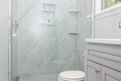 Example of a large transitional master stone slab marble floor and gray floor bathroom design in Other with raised-panel cabinets, gray cabinets, a one-piece toilet, blue walls, an integrated sink, solid surface countertops and white countertops