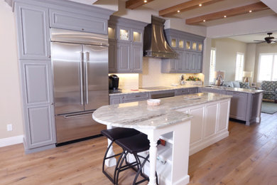 This is an example of a large transitional l-shaped eat-in kitchen in Miami with a double-bowl sink, raised-panel cabinets, grey cabinets, white splashback, cement tile splashback, stainless steel appliances, light hardwood floors and with island.