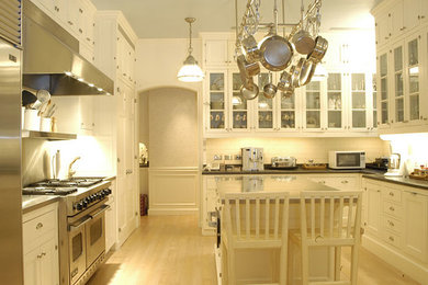 Kitchen - light wood floor kitchen idea in New York with glass-front cabinets, white cabinets, white backsplash, stainless steel appliances and an island