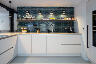 Inspiration for a medium sized modern cream and black kitchen/diner in London with a built-in sink, all styles of cabinet, white cabinets, quartz worktops, blue splashback, metro tiled splashback, stainless steel appliances, light hardwood flooring, a breakfast bar and white worktops.