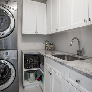 Modelo de cuarto de lavado en L, tradicional renovado, de tamaño medio, con fregadero bajoencimera, armarios estilo shaker, puertas de armario blancas, encimera de granito, paredes blancas, suelo de baldosas de porcelana y lavadora y secadora apiladas