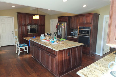 Large trendy u-shaped medium tone wood floor enclosed kitchen photo in Columbus with an island, raised-panel cabinets, brown cabinets, granite countertops, multicolored backsplash, glass sheet backsplash, stainless steel appliances and an undermount sink