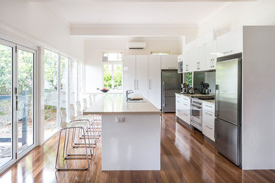 Photo of a mid-sized contemporary single-wall eat-in kitchen in Brisbane with a drop-in sink, flat-panel cabinets, white cabinets, marble benchtops, white splashback, ceramic splashback, white appliances, dark hardwood floors, with island and brown floor.