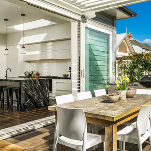 Foto de cocina de galera, costera, abierta, con fregadero bajoencimera, armarios con paneles lisos, puertas de armario blancas, salpicadero blanco, salpicadero de metal, suelo de madera oscura, una isla, suelo marrón y electrodomésticos de acero inoxidable