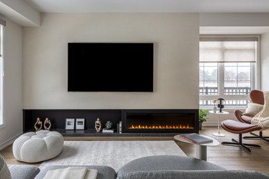 Trendy medium tone wood floor and brown floor family room photo in Toronto with beige walls, a standard fireplace and a plaster fireplace