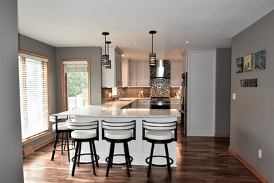 Example of a mid-sized transitional u-shaped medium tone wood floor open concept kitchen design in Milwaukee with a double-bowl sink, recessed-panel cabinets, gray cabinets, granite countertops, green backsplash, glass tile backsplash, stainless steel appliances and a peninsula
