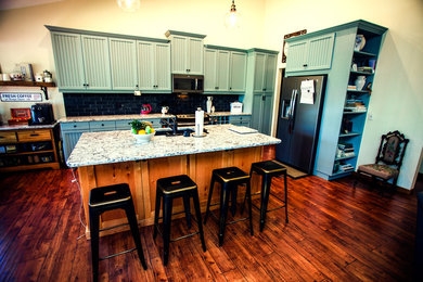 Example of a large eclectic l-shaped medium tone wood floor and brown floor open concept kitchen design in Orlando with an undermount sink, louvered cabinets, blue cabinets, granite countertops, black backsplash, stone slab backsplash, stainless steel appliances and an island