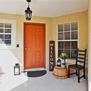 Inredning av en eklektisk entré, med beige väggar, betonggolv, en enkeldörr, en orange dörr och grått golv