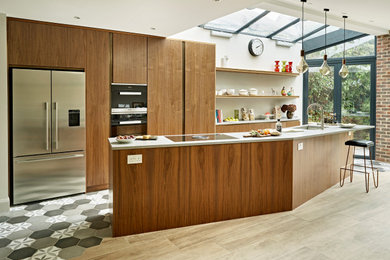 Photo of a medium sized galley open plan kitchen in London with an integrated sink, flat-panel cabinets, dark wood cabinets, concrete worktops, stainless steel appliances, porcelain flooring, an island, multi-coloured floors, grey worktops and a vaulted ceiling.