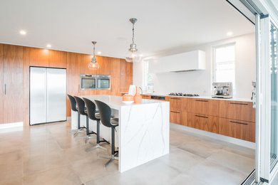 Large contemporary l-shaped kitchen in Sydney with flat-panel cabinets, medium wood cabinets, stainless steel appliances, with island, grey floor and white benchtop.
