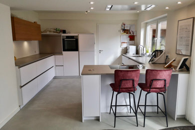 Offene, Mittelgroße Moderne Küche in L-Form mit integriertem Waschbecken, flächenbündigen Schrankfronten, weißen Schränken, Laminat-Arbeitsplatte, Küchenrückwand in Weiß, Küchengeräten aus Edelstahl, Halbinsel und grauer Arbeitsplatte in Essen