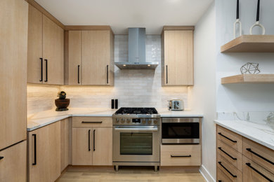 Large minimalist u-shaped light wood floor and brown floor eat-in kitchen photo in Chicago with flat-panel cabinets, light wood cabinets, quartz countertops, white backsplash, subway tile backsplash, stainless steel appliances, an island and white countertops