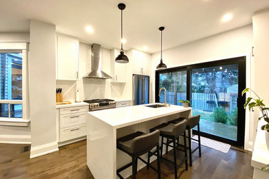 Example of a mid-sized trendy galley medium tone wood floor and brown floor eat-in kitchen design in Toronto with an undermount sink, recessed-panel cabinets, white cabinets, quartz countertops, white backsplash, quartz backsplash, stainless steel appliances, an island and white countertops