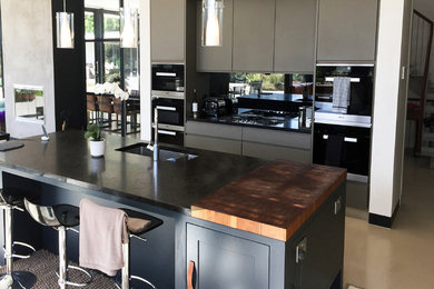 Photo of a large contemporary kitchen/diner in London with flat-panel cabinets, grey cabinets, granite worktops, concrete flooring, an island and beige floors.