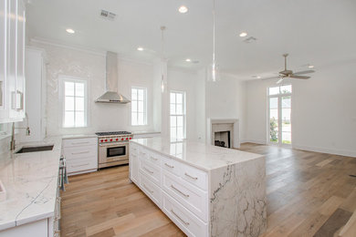 Mid-sized transitional l-shaped open plan kitchen in New Orleans with an undermount sink, shaker cabinets, white cabinets, marble benchtops, white splashback, ceramic splashback, light hardwood floors, with island, brown floor and grey benchtop.