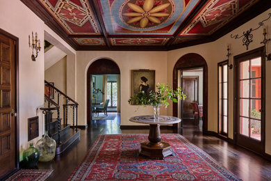 Huge tuscan dark wood floor and brown floor foyer photo in Los Angeles with beige walls and a dark wood front door
