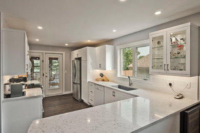 Inspiration for a mid-sized transitional laminate floor and brown floor eat-in kitchen remodel in Other with an undermount sink, shaker cabinets, white cabinets, quartz countertops, white backsplash, porcelain backsplash, stainless steel appliances, a peninsula and white countertops