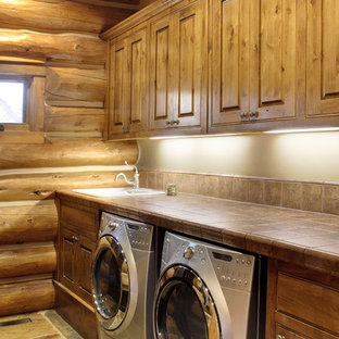 This is an example of a medium sized rustic single-wall separated utility room in Seattle with a built-in sink, raised-panel cabinets, dark wood cabinets, tile countertops, beige walls, a side by side washer and dryer, slate flooring, beige floors and brown worktops.
