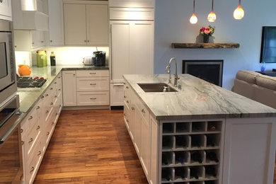 This is an example of a large transitional l-shaped open plan kitchen in Sacramento with an undermount sink, shaker cabinets, white cabinets, marble benchtops, panelled appliances, dark hardwood floors, with island, brown floor, white splashback and grey benchtop.