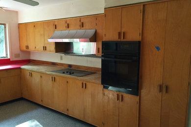Example of a mid-sized 1960s l-shaped enclosed kitchen design in Boston with a drop-in sink, flat-panel cabinets, light wood cabinets, wood countertops and black appliances
