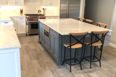 Inspiration for a large cottage l-shaped porcelain tile eat-in kitchen remodel in New York with a farmhouse sink, recessed-panel cabinets, white cabinets, quartzite countertops, white backsplash, ceramic backsplash, stainless steel appliances and an island