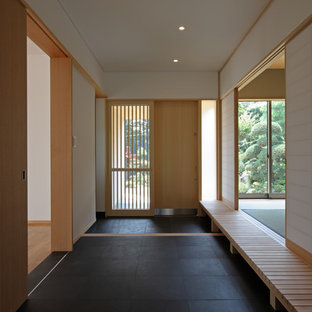 他の地域の大きい引き戸アジアンスタイルのおしゃれな玄関ロビー (白い壁、淡色木目調のドア、黒い床) の写真