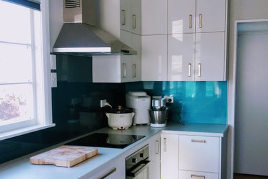 This is an example of a mid-sized contemporary galley eat-in kitchen in Other with a single-bowl sink, flat-panel cabinets, white cabinets, laminate benchtops, blue splashback, glass sheet splashback, black appliances, vinyl floors, no island and brown floor.