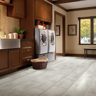他の地域の大きいトラディショナルスタイルのおしゃれな洗濯室 (エプロンフロントシンク、レイズドパネル扉のキャビネット、濃色木目調キャビネット、ソープストーンカウンター、ベージュの壁、磁器タイルの床、左右配置の洗濯機・乾燥機、グレーの床) の写真
