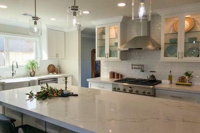Mid-sized transitional porcelain tile and gray floor open concept kitchen photo in Los Angeles with a farmhouse sink, shaker cabinets, white cabinets, quartz countertops, white backsplash, subway tile backsplash, stainless steel appliances, an island and white countertops