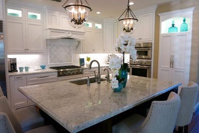 Kitchen - mid-sized traditional l-shaped medium tone wood floor kitchen idea in Portland with an undermount sink, recessed-panel cabinets, granite countertops, white backsplash, ceramic backsplash, stainless steel appliances and an island