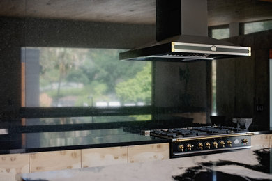 ロサンゼルスにあるラグジュアリーな広いコンテンポラリースタイルのおしゃれなアイランドキッチン (フラットパネル扉のキャビネット、黒いキッチンパネル、御影石のキッチンパネル、黒い調理設備、マルチカラーのキッチンカウンター) の写真